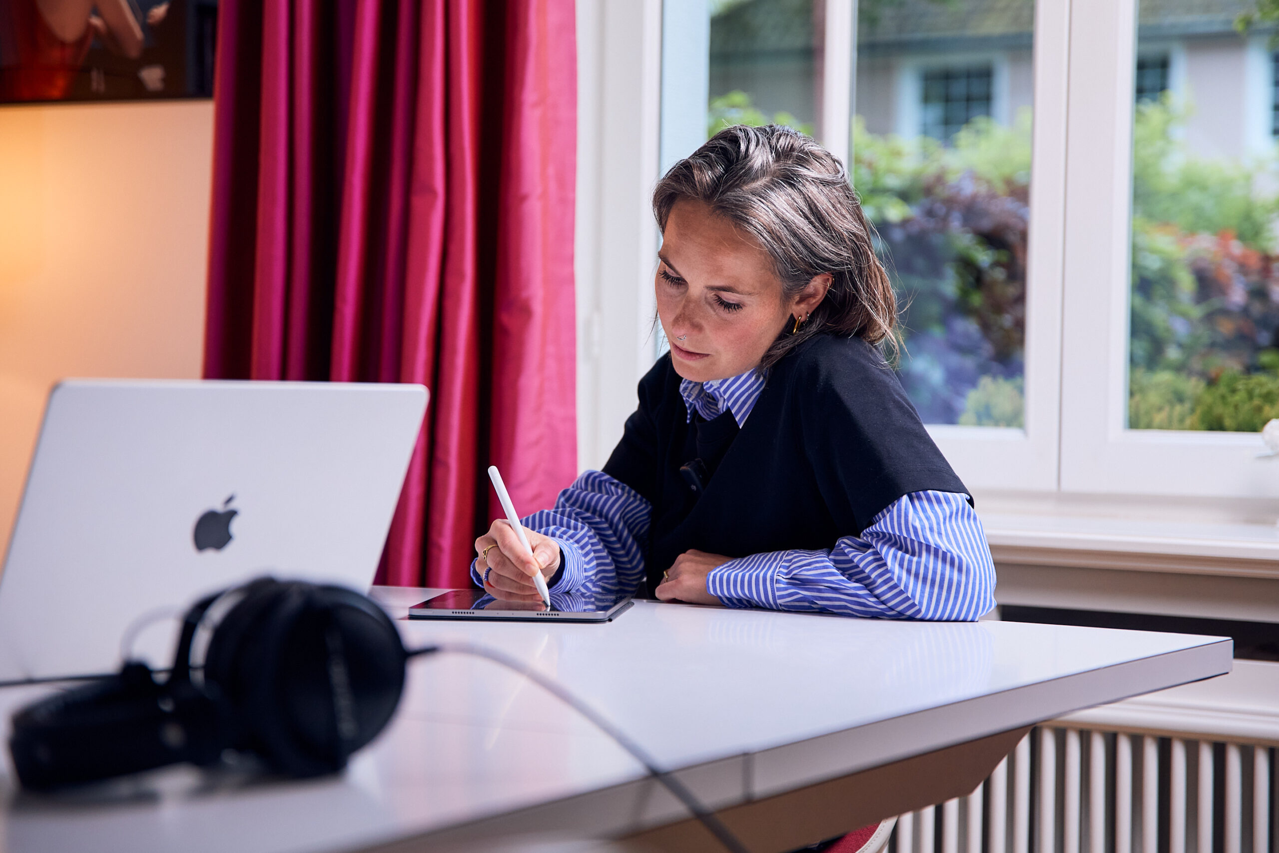 Behind the Scenes – Kollegin arbeitet mit Stift am Tablet, Fensterblick ins Grüne
