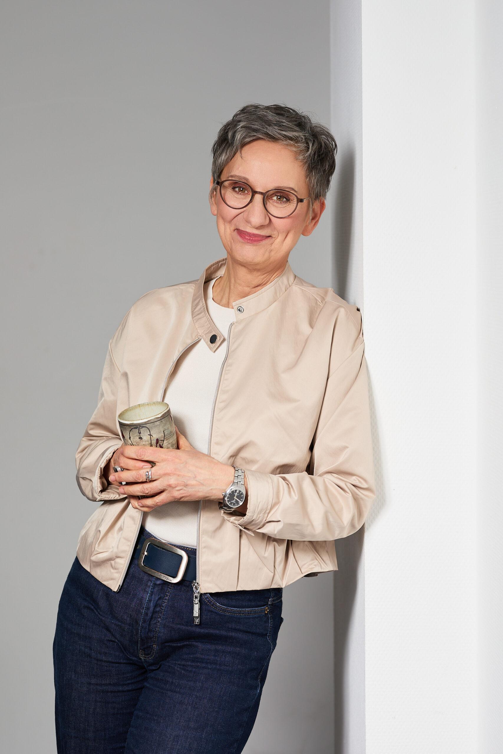 Personal-Branding-Shooting Eva Kräling – stehend an Wand gelehnt mit Kaffeetasse